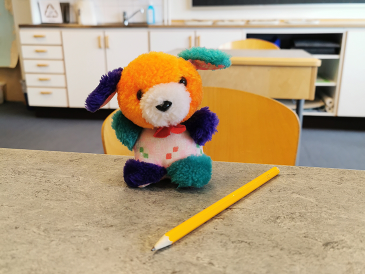 Ett foto på ett färgglatt kramdjur som sitter på en skolbänk.