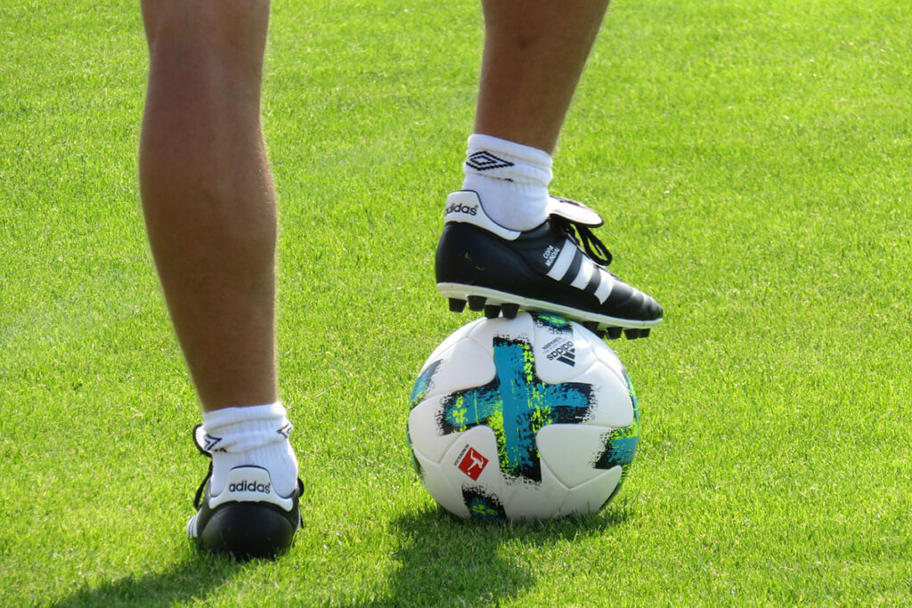 I bild syns två ben och en fotboll på en gräsplan.