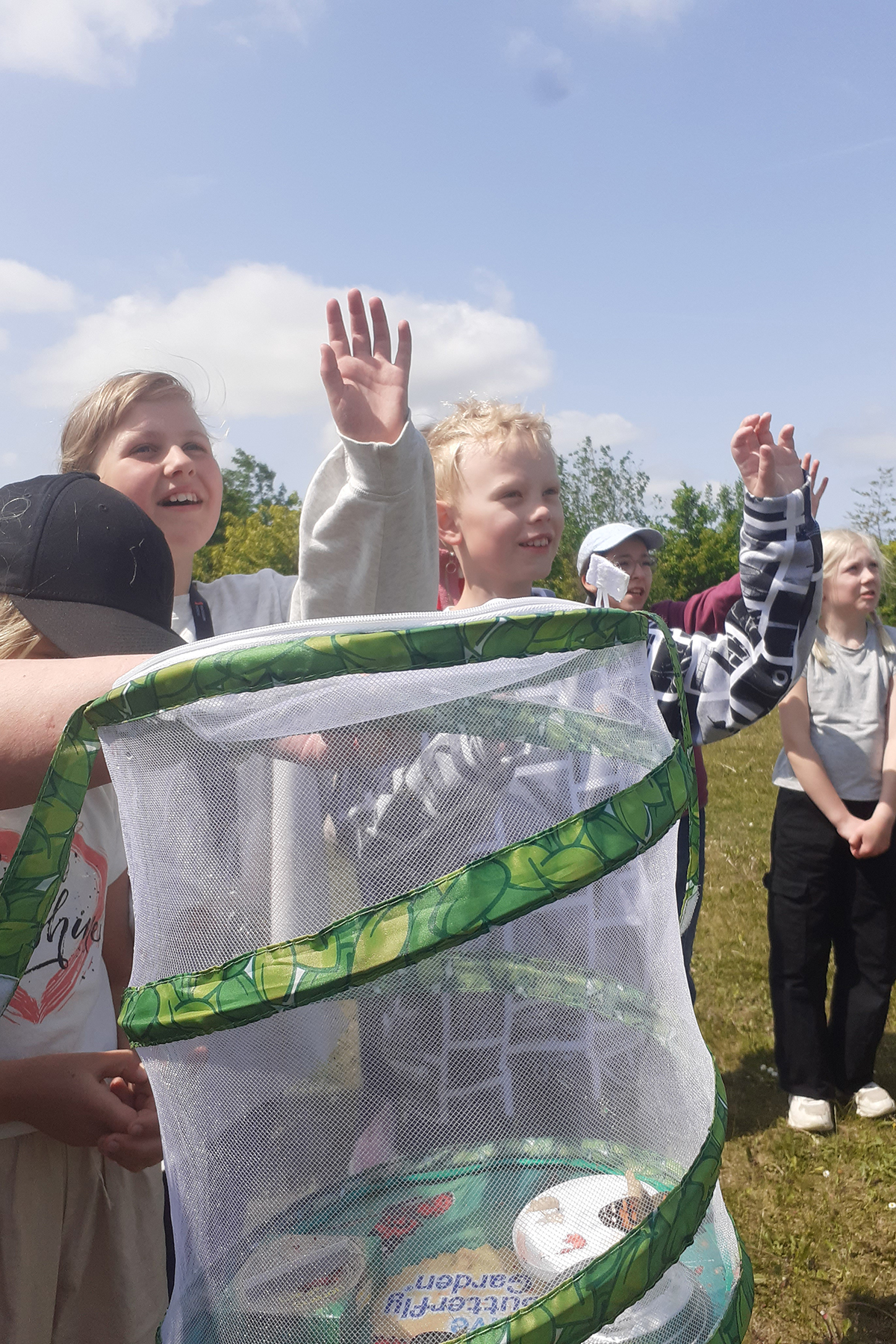 Elever som vinkar hejdå till fjärilarna. En håv i förgrunden.